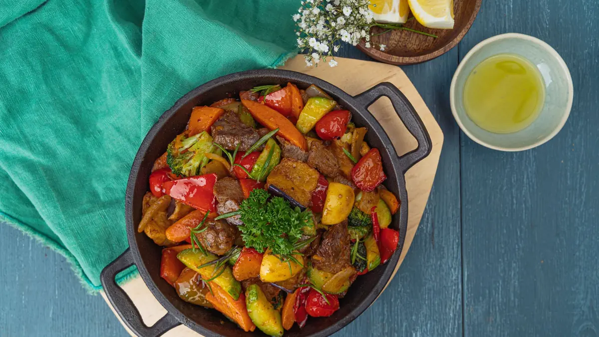 Oksekød stegt med rød og gul peberfrugt, gulerod, squash og broccoli i en sort støbejernspande, set ovenfra