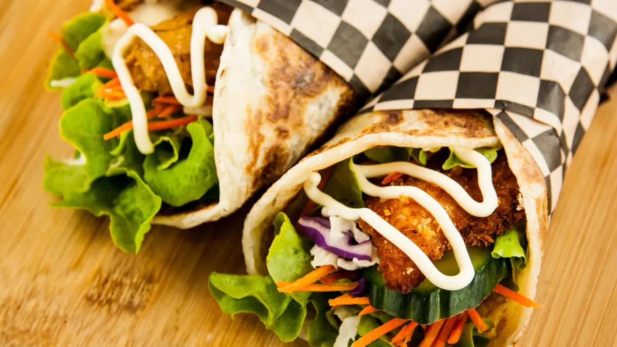 Wraps med kylling, salat, agurk og gulerod skåret over på et bræt