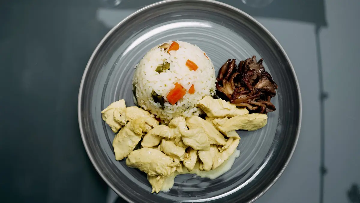 Strimlet kyllingebryst i lys sauce anrettet med ris og stegte svampe på en grå tallerken