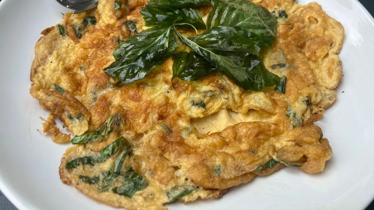 Gyldenbrun omelet med grønne blade bagt ind i æggemassen, toppet med friske basilikumblade på en hvid tallerken