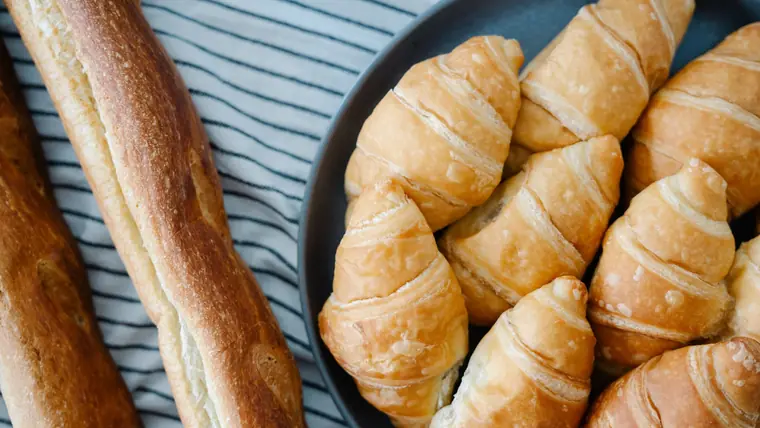 Croissanter på en mørk tallerken ved siden af to sprøde baguetter på en stribet dug, set ovenfra