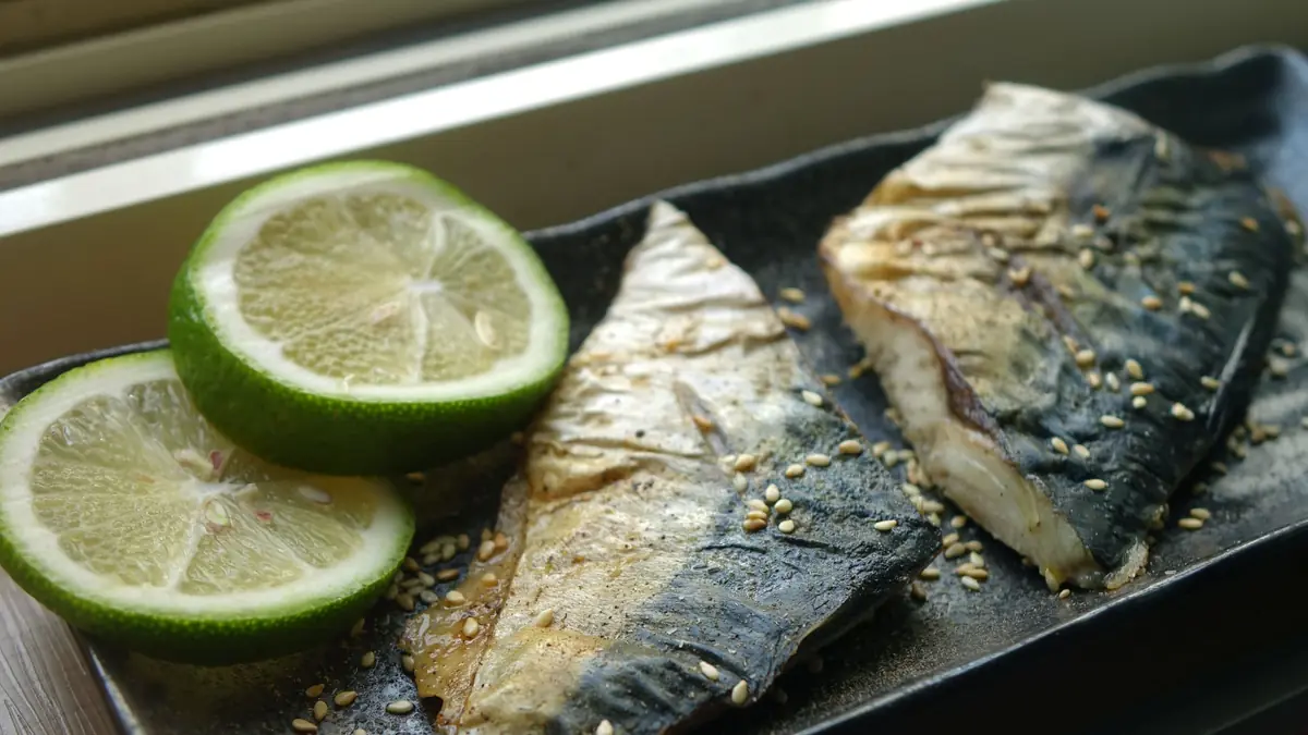 To grillede makrelfileter med sprødt skind, limeskiver og sesamfrø på et mørkt fad
