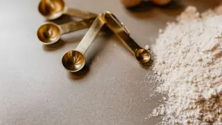 Måleskeer ved siden af mel og æg på et køkkenbord under bagning