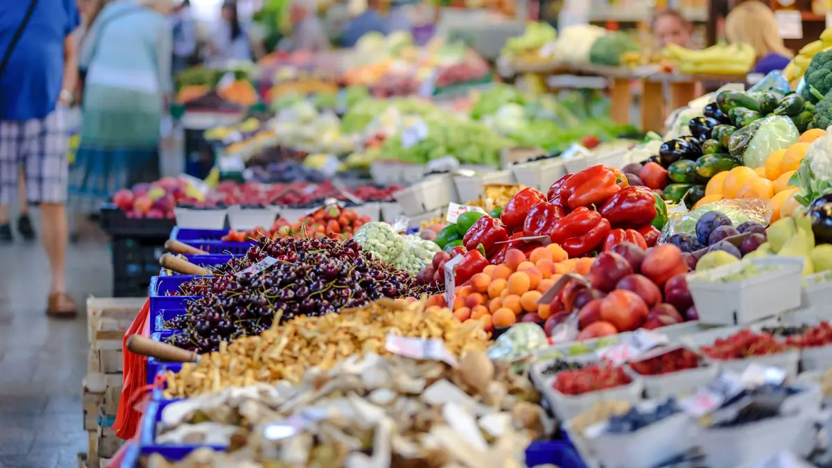 Lange rækker af markedsboder i en overdækket hal med kirsebær, kantareller, peberfrugter, abrikoser og bær i kasser