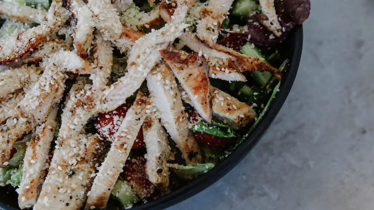 Salat med grillet kylling, friske grøntsager og drysset kerner i en mørk skål