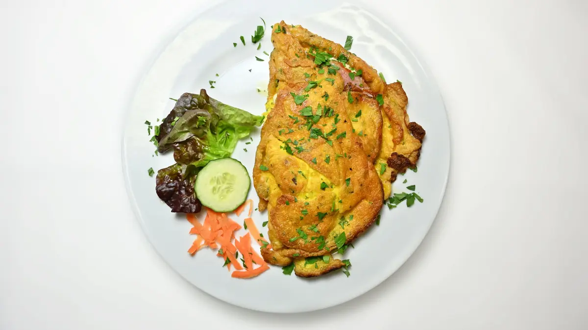 Æggekage på en hvid tallerken med frisk salat, agurk og gulerod, set oppefra