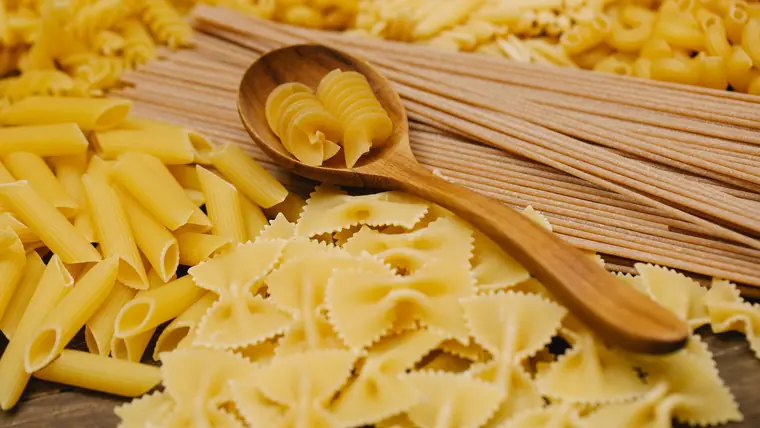 Forskellige slags rå pasta i skåle med en træske ved siden af