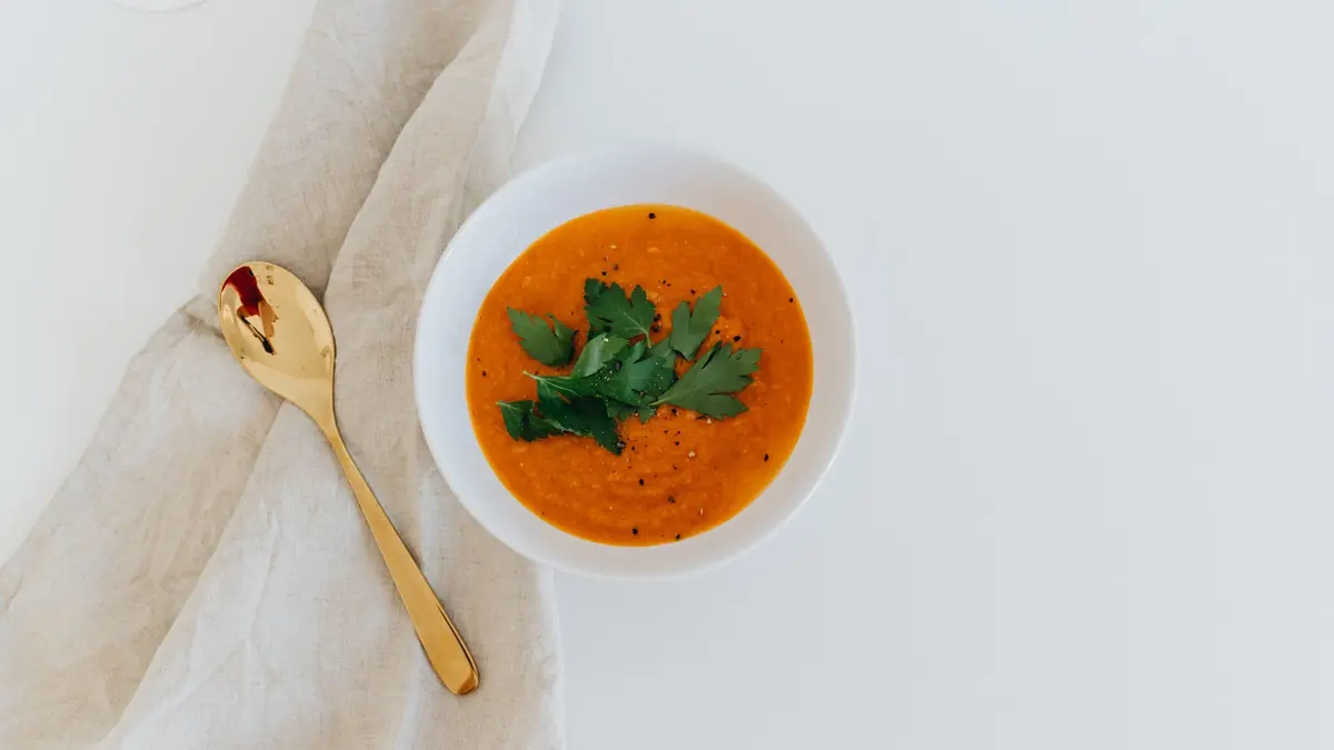 Cremet orange gulerodssuppe i en lys skål med en gylden ske ved siden af