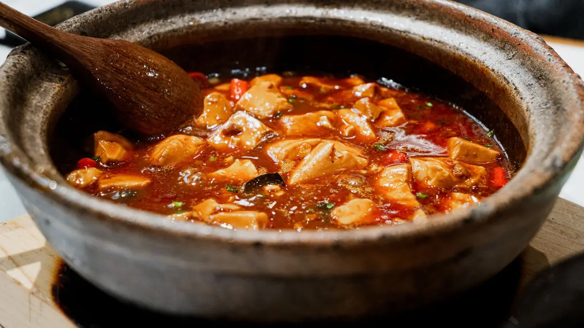 Tofu i en rød tomatgryde med peberfrugt, serveret i en rustik lerpotte med træske