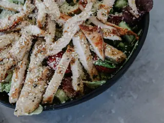 Salat med grillet kylling, friske grøntsager og drysset kerner i en mørk skål