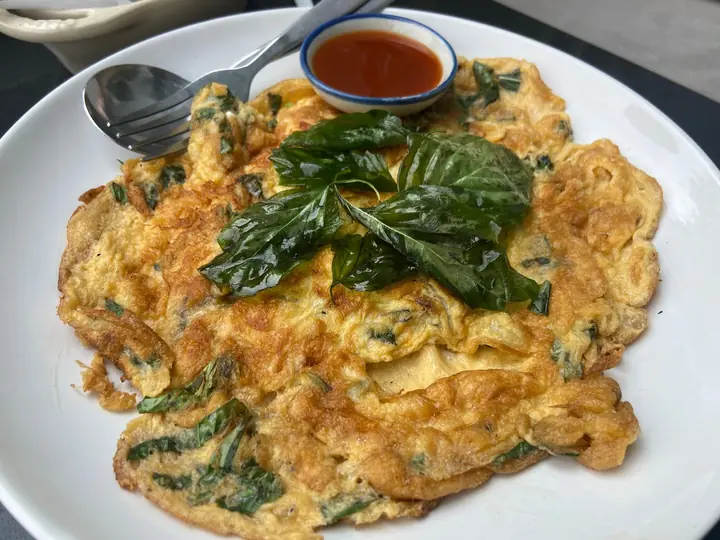 Gyldenbrun omelet med grønne blade bagt ind i æggemassen, toppet med friske basilikumblade på en hvid tallerken
