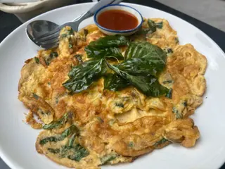 Gyldenbrun omelet med grønne blade bagt ind i æggemassen, toppet med friske basilikumblade på en hvid tallerken