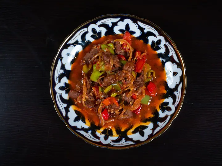Oksekød i krydret tomatsauce med grøn og rød peberfrugt i en mønstret skål, set ovenfra
