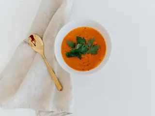 Cremet orange gulerodssuppe i en lys skål med en gylden ske ved siden af
