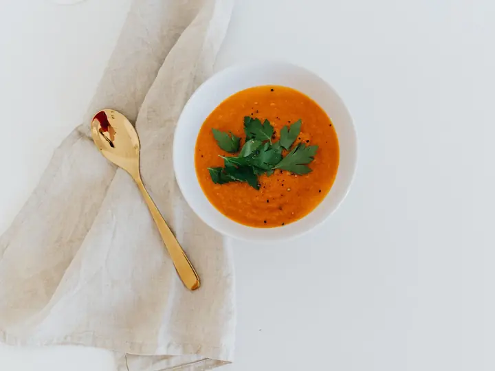 Cremet orange gulerodssuppe i en lys skål med en gylden ske ved siden af