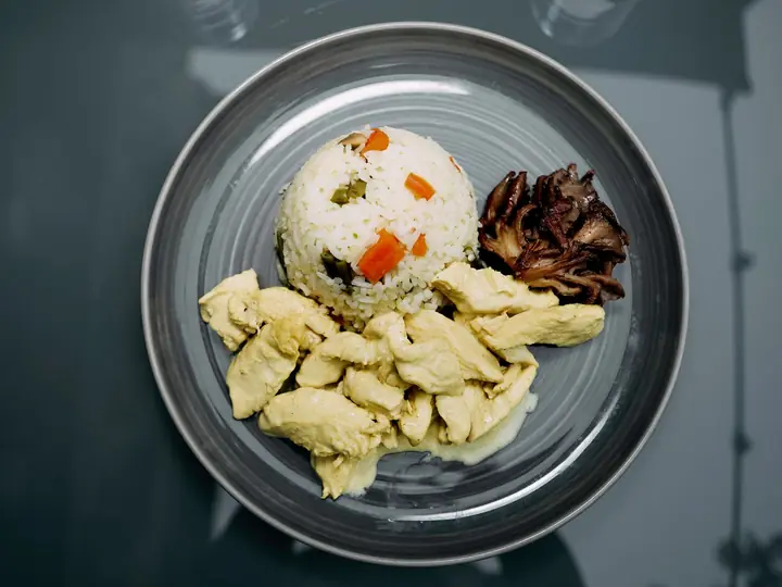 Strimlet kyllingebryst i lys sauce anrettet med ris og stegte svampe på en grå tallerken